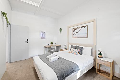 a white bedroom with a large bed and a table at Rustic Queen Room - Seconds to Stores & Eateries - Shared Bathroom in Sydney