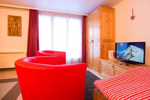 uma sala de estar com duas cadeiras vermelhas e uma televisão em MOM - Alpine Boutique Apartments, Grindelwald gletscher, Eiger View Terrace Studio em Grindelwald