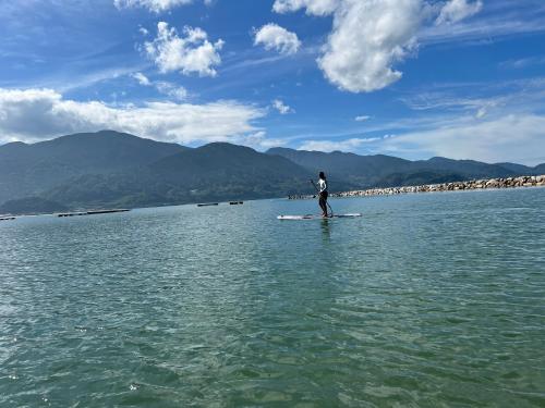 a man standing on a paddle board in the water at ITOSHIMA SDGs Village Chikyu MIRAI -海の大パノラマ-全室オーシャンビューのドームテント in Itoshima