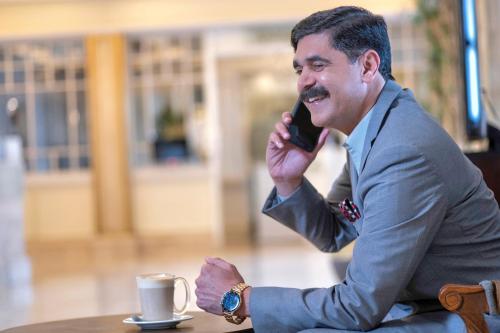 a man sitting at a table talking on a cell phone at Pearl Continental Hotel, Bhurban in Bhurban