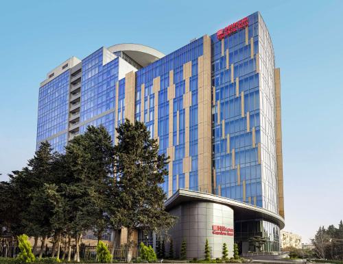 a tall glass building with a tree in front of it at Hilton Garden Inn Baku in Baku