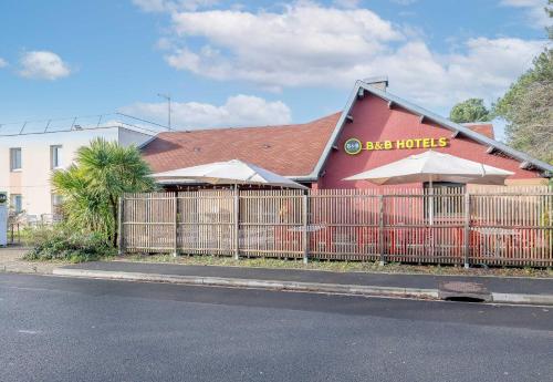 a building with a fence in front of a restaurant at B&B HOTEL Bordeaux Mérignac Cadera Aéroport in Mérignac