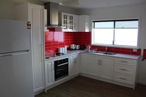 a kitchen with white cabinets and red tiles at Cosy 3 bedroom cottage in the centre of Kingscote in Kingscote