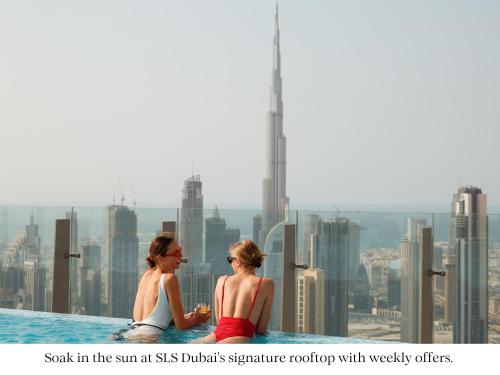 two women sitting on the edge of a swimming pool at the shibuya district at SLS Dubai Hotel & Residences in Dubai