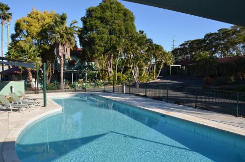 a swimming pool with a fence and trees at Puffers Inn in Loganholme