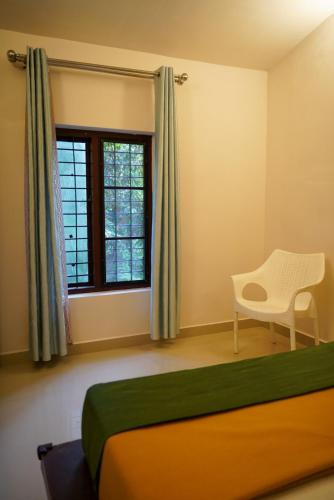 a bedroom with a bed and a chair and a window at Misty Hills Cabin in Wayanad
