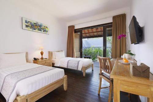 a bedroom with two beds and a desk with a television at Royal Regantris Villa Karang in Gili Air