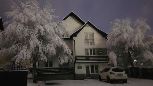 a white car parked in front of a house covered in snow at Willa Rodzinna in Tylicz