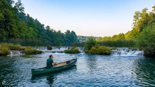 a man in a canoe on a river with a waterfall at Bed & Breakfast Zeleni Kut in Gornji Zvečaj