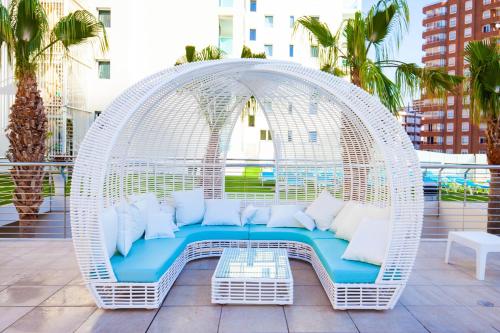 a white wicker swing on a balcony with white pillows at Port Benidorm Hotel & Spa 4* Sup in Benidorm
