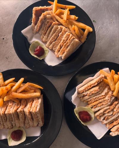 three black plates with sandwiches and french fries on them at Cafekush tosh in Tosh