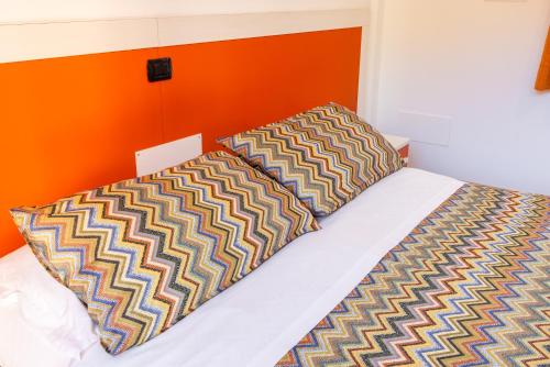 a bed with two pillows and an orange wall at Spluga "Relax & Apartaments" by Alfio Colombo in Sorico