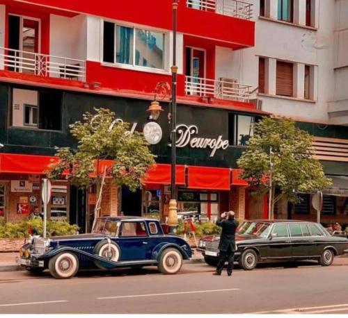two old cars parked on a street in front of a building at Hotel D'Europe Centre Ville in Kenitra