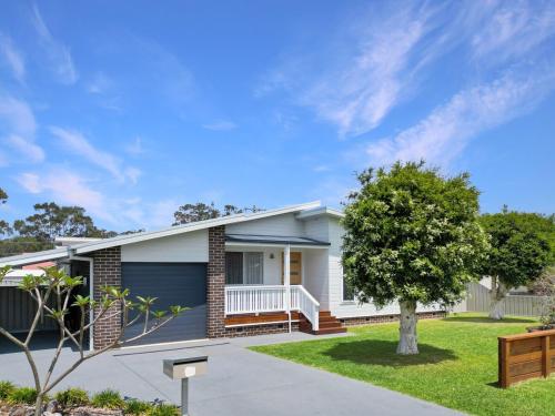 a white house with a blue garage at Paperbark Cottage in Callala Bay