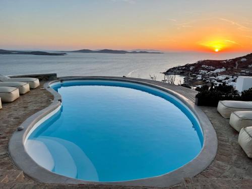 a swimming pool in front of a beach at sunset at Villa Tavani Agios Ioannis Mykonos in Agios Ioannis Mykonos