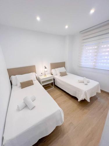 two beds in a white room with a window at El rincón de María in Torremolinos