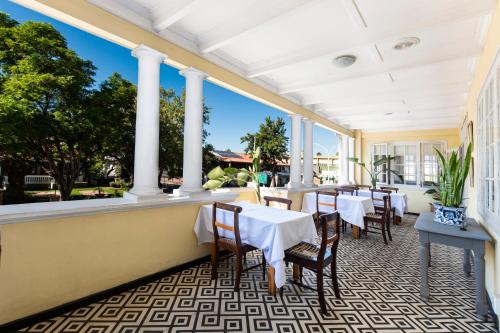 a restaurant with white tables and chairs and columns at Queen's Hotel by BON Hotels in Oudtshoorn