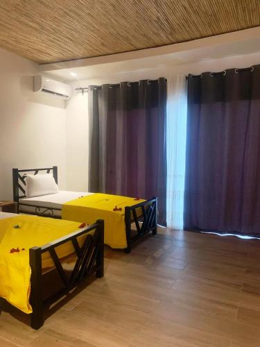 two beds in a room with curtains and wooden floors at Résidence Kanissa in Cap Skirring