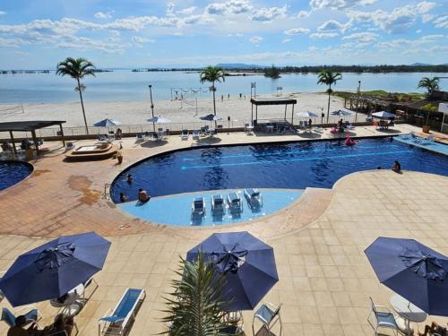 a swimming pool with chairs and umbrellas next to a beach at Apartamento em Arraial do Cabo in Arraial do Cabo