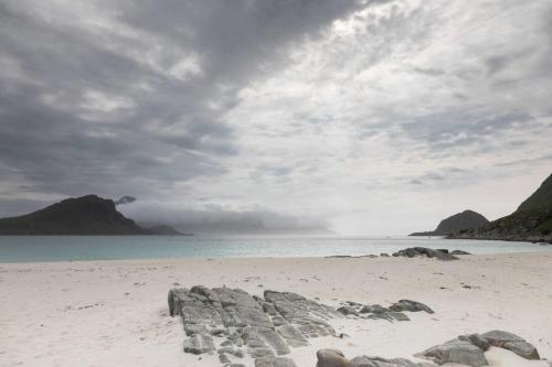 a beach with rocks on the sand and the water at Charming house in fjord Lofoten in Slydalen