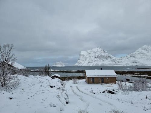a house in a snowy field with mountains in the background at Magic views and walking distance to best beaches in Leknes
