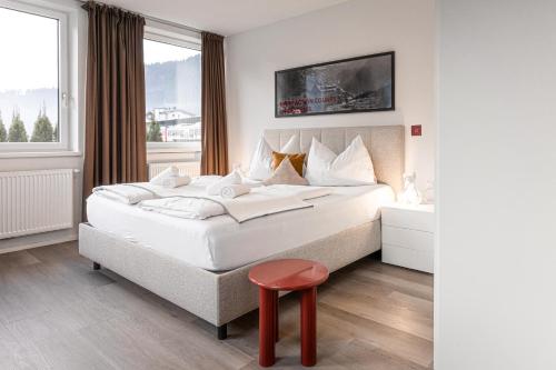 a bedroom with a large white bed with a red stool at Lebe`schlitters - Das Ferienapartmenthaus im Zillertal in Schlitters