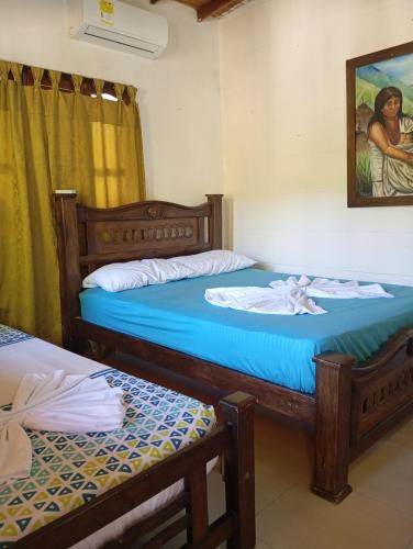 a bedroom with two beds and a painting on the wall at Hostal Los Wichos in Minca