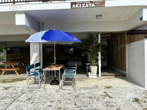 a table and chairs with an umbrella in front of a building at Guest House AKIZATA ゲストハウス アキザタ in Zamami