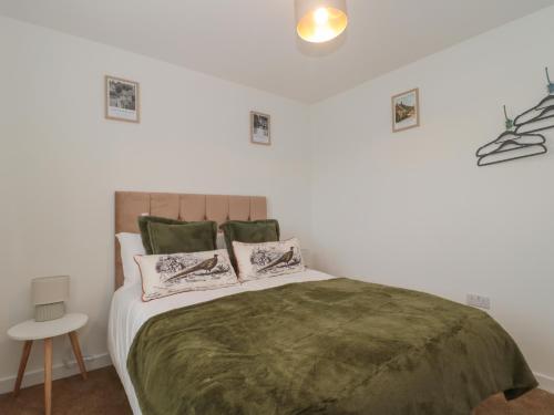 a bedroom with a bed with a green blanket and pillows at Cotswold Outlet Coach House in Tewkesbury