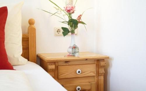 a vase with flowers on a wooden table next to a bed at Fürstenhof Landgasthaus & Hotel in Erfurt
