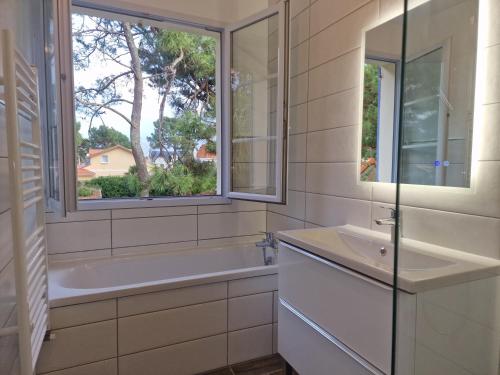 La salle de bains est pourvue d'un lavabo, d'une baignoire et d'une fenêtre. dans l'établissement Les Pins grand duplex T5 avec jardin les plages à pied, à Pornichet