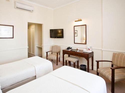 a hotel room with two beds and a desk and a mirror at Queen's Hotel by BON Hotels in Oudtshoorn