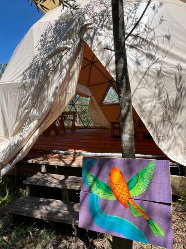 a painting of a colorful bird sitting on a table next to a tent at La Templanza EcoGlamping in Rincón de los Oliveras