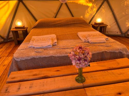 a bed in a tent with towels and a vase of flowers at La Templanza EcoGlamping in Rincón de los Oliveras