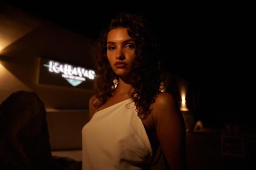 a woman in a white dress standing in a dark room at Mykonos Bay Resort & Villas in Mýkonos City