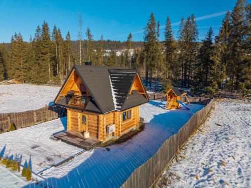 a log cabin with a black roof in the snow at Domki Biała i Czarna Owca in Witów