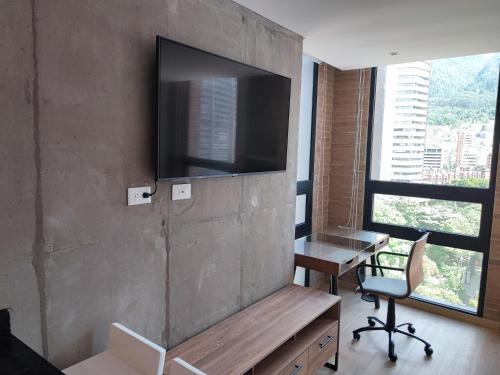 a room with a television on a wall with a table and a desk at ApartaSuite Centro Internacional in Bogotá
