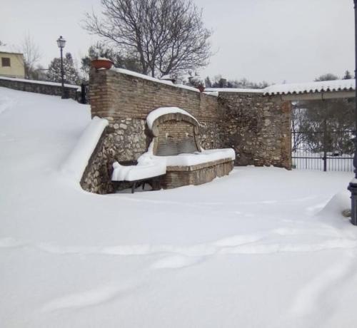 a snow covered bench in front of a brick wall at LA BAITA di Ornaro Alto Rieti - oasi di pace tra Roma e Terminillo in Ornaro