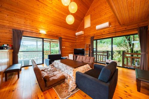 a living room with a table and couches and windows at 天然温泉露天風呂付コテージ山樹荘 in Hita