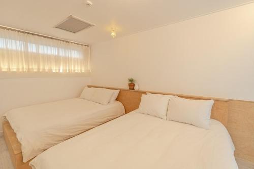 two beds in a room with white walls and a window at Jeju Byeolkkum Pension in Jeju