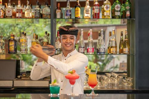 a man is standing behind a bar with a drink at Prime Plaza Hotel Sanur – Bali in Sanur