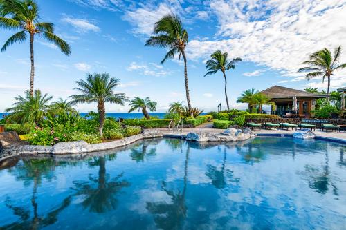a swimming pool with palm trees and a house at 14B Halii Kai in Waikoloa