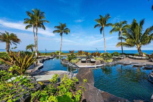 a resort pool with palm trees and the ocean at 14B Halii Kai in Waikoloa