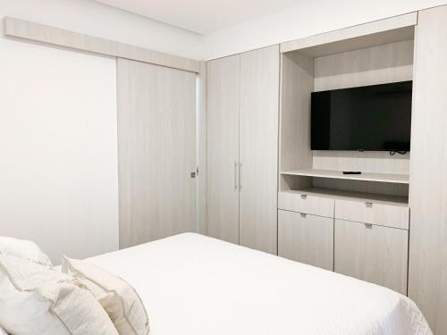 a white bedroom with a tv and a bed at Airbnb Guayaquil, Mall del Sol, Piso alto in Guayaquil