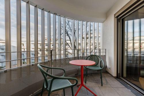 a balcony with two chairs and a red table in front of windows at Brucklyn Suites in Erlangen