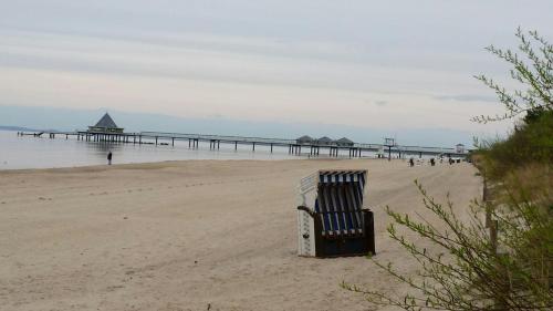 a chair sitting on a beach with a pier at Pension "Am Fischerweg" in Heringsdorf