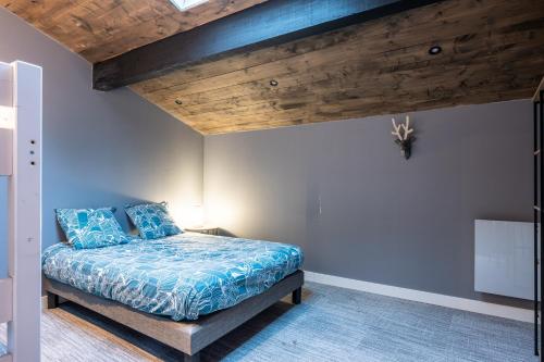a bedroom with a bed with blue sheets and wooden ceilings at Bienvenue Chez Les Trutes in Modane