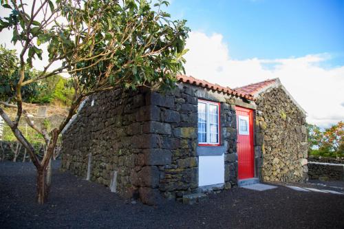 a stone house with a red door and a tree at Aldeia Dos Caldeirões in São Mateus