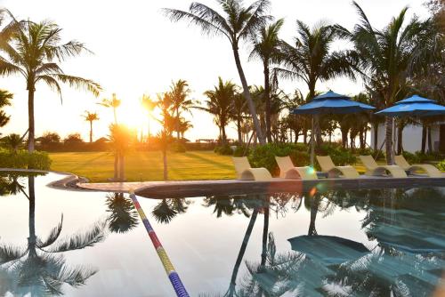 a pool with chairs and umbrellas and palm trees at The Vista Beach Resort Phan Thiết in Phan Thiet