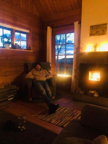 a man sitting on a couch in a living room with a fireplace at Kustnära hus med utsikt över havet och karlsöarna in Klintehamn